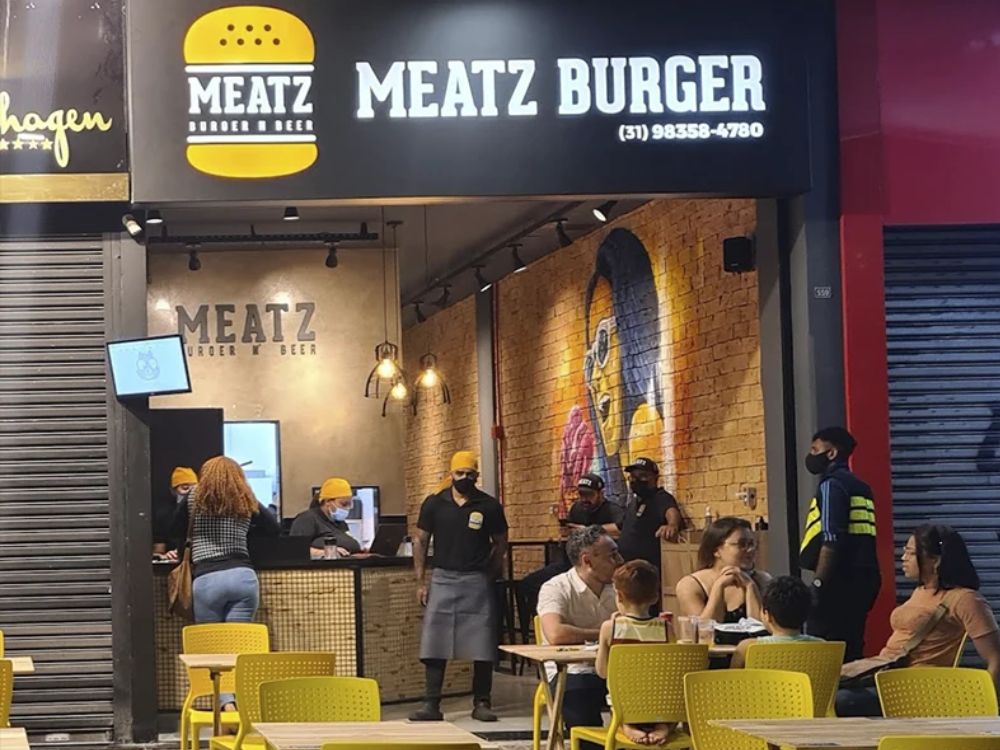 Fachada moderna de unidade da Meatz Burger com mesas externas, representando uma franquia de hambúrguer artesanal com ambiente descontraído.