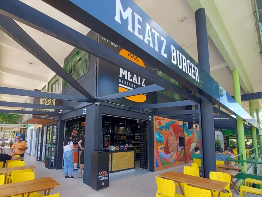 Fachada moderna de unidade da Meatz Burger com mesas externas, representando uma franquia de hambúrguer artesanal com ambiente descontraído.