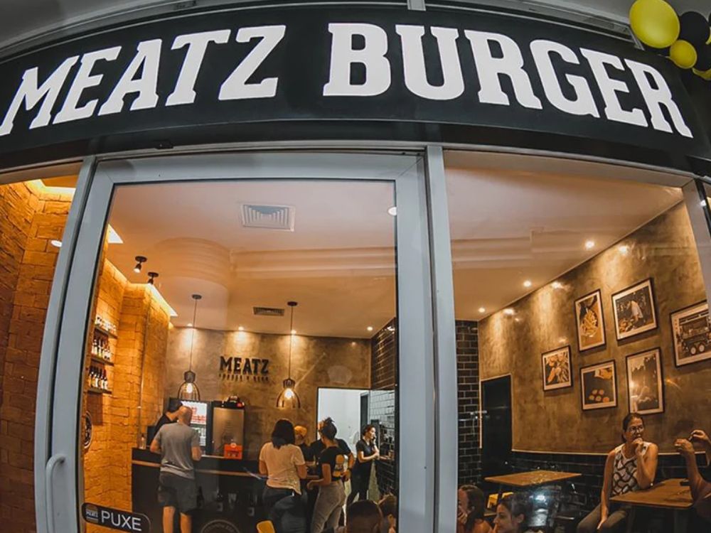Fachada de loja Meatz Burger com interior acolhedor e clientes satisfeitos, reforçando a proposta da franquia de hambúrguer artesanal.