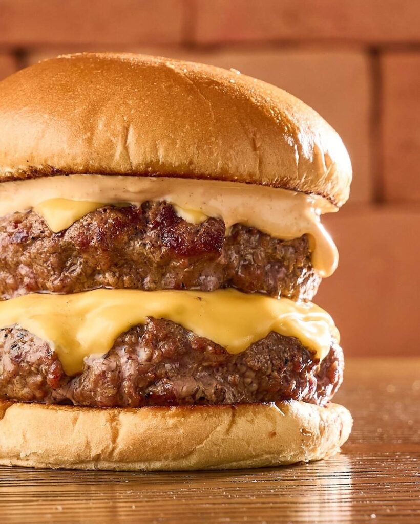 Hambúrguer artesanal duplo com queijo derretido e molho especial, símbolo irresistível do Dia Nacional do Hambúrguer.